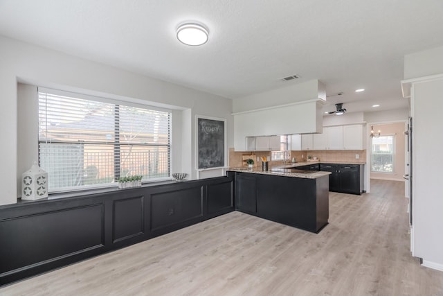 kitchen featuring white cabinetry, kitchen peninsula, light stone countertops, and light wood-type flooring