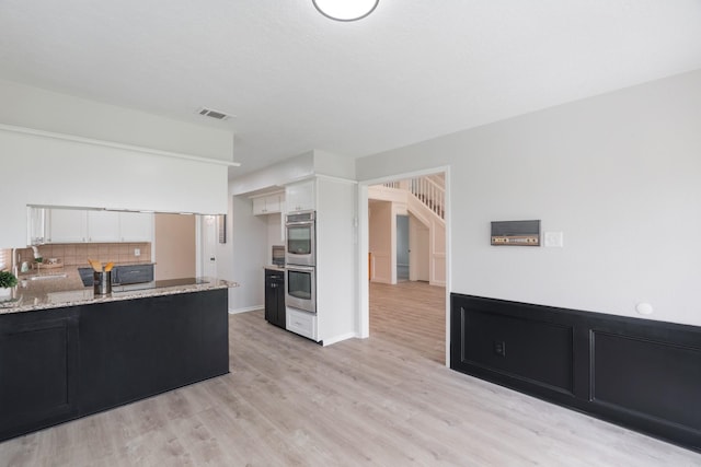 kitchen featuring double oven, sink, white cabinets, decorative backsplash, and light stone countertops