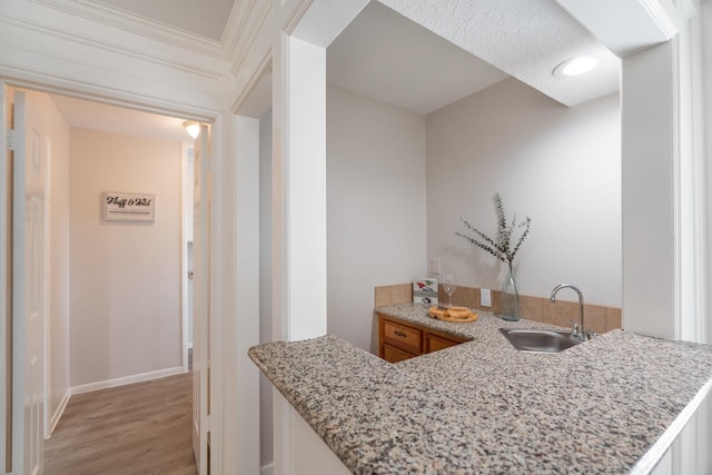 kitchen featuring light stone counters, kitchen peninsula, sink, and light hardwood / wood-style flooring