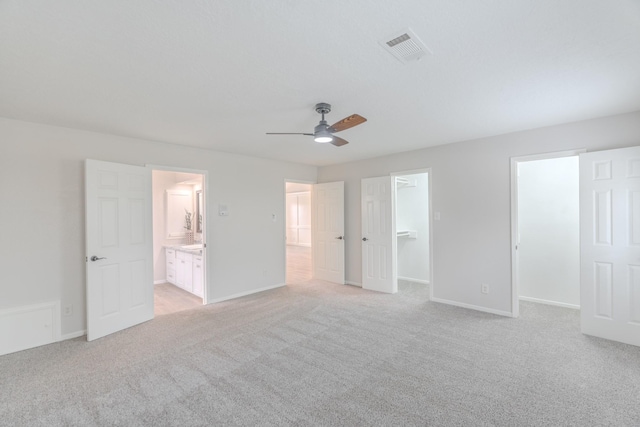 unfurnished bedroom featuring light carpet, ensuite bath, ceiling fan, and a spacious closet