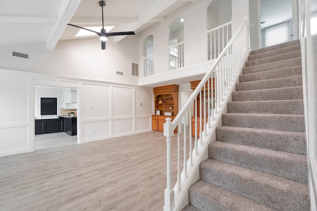 staircase with beam ceiling, high vaulted ceiling, hardwood / wood-style floors, and ceiling fan