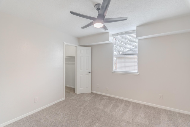 unfurnished bedroom with a walk in closet, light carpet, a textured ceiling, a closet, and ceiling fan