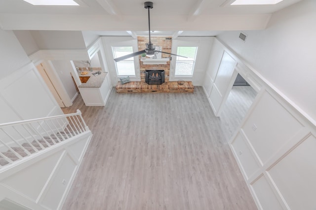 unfurnished living room with beam ceiling, a skylight, light hardwood / wood-style floors, and ceiling fan