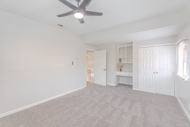 unfurnished bedroom featuring ceiling fan, light colored carpet, built in desk, and a closet