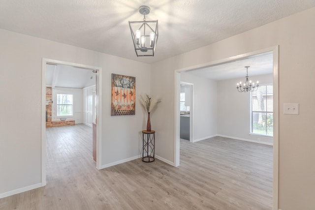 spare room with a notable chandelier, a textured ceiling, and light wood-type flooring