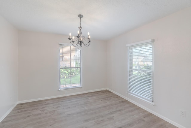 unfurnished room featuring a notable chandelier, a textured ceiling, and light wood-type flooring