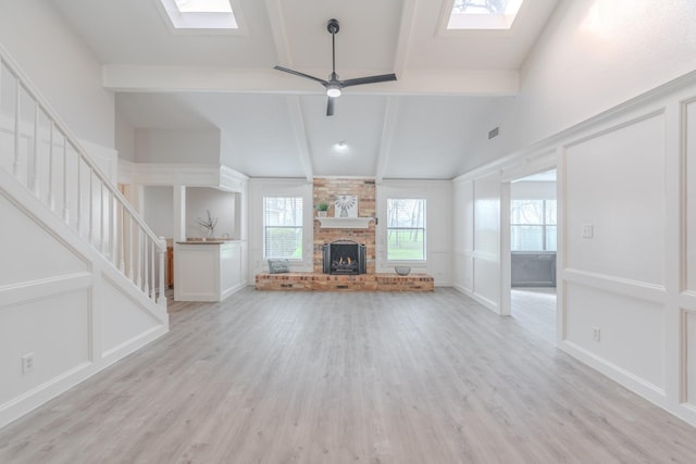 unfurnished living room featuring a fireplace, beam ceiling, a skylight, and light hardwood / wood-style flooring