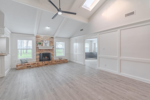 unfurnished living room with light hardwood / wood-style flooring, a skylight, a fireplace, and beamed ceiling