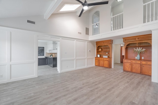 unfurnished living room featuring lofted ceiling with skylight, light hardwood / wood-style floors, and ceiling fan