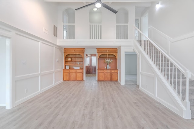 unfurnished living room featuring ceiling fan, light wood-type flooring, and a high ceiling