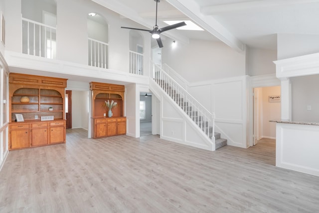 unfurnished living room with ceiling fan, beam ceiling, high vaulted ceiling, and light hardwood / wood-style flooring