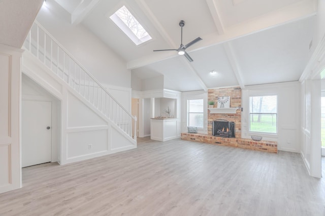 unfurnished living room featuring a brick fireplace, beam ceiling, light hardwood / wood-style floors, and ceiling fan