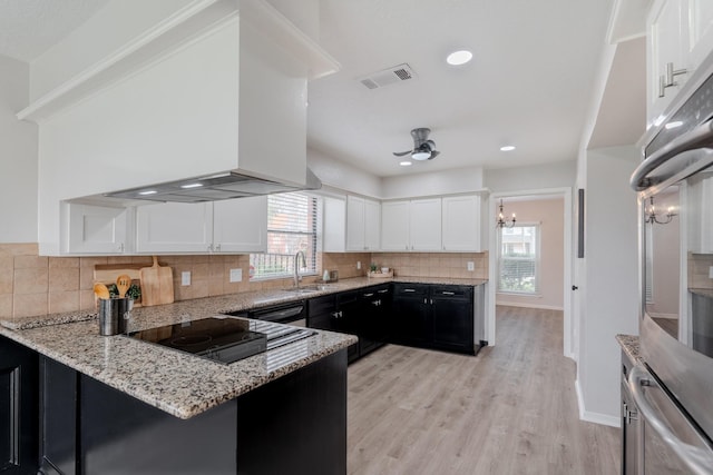 kitchen with white cabinetry, sink, light stone counters, black appliances, and wall chimney exhaust hood