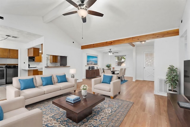 living room featuring light hardwood / wood-style flooring, ceiling fan, high vaulted ceiling, washing machine and clothes dryer, and beamed ceiling