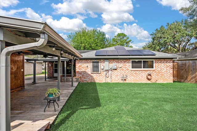 rear view of property featuring a wooden deck, a lawn, and solar panels