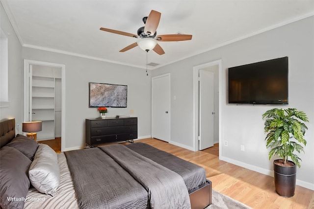 bedroom with ornamental molding, a walk in closet, ceiling fan, light hardwood / wood-style floors, and a closet