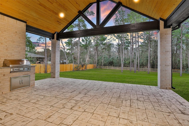 patio terrace at dusk with a grill, a yard, and exterior kitchen