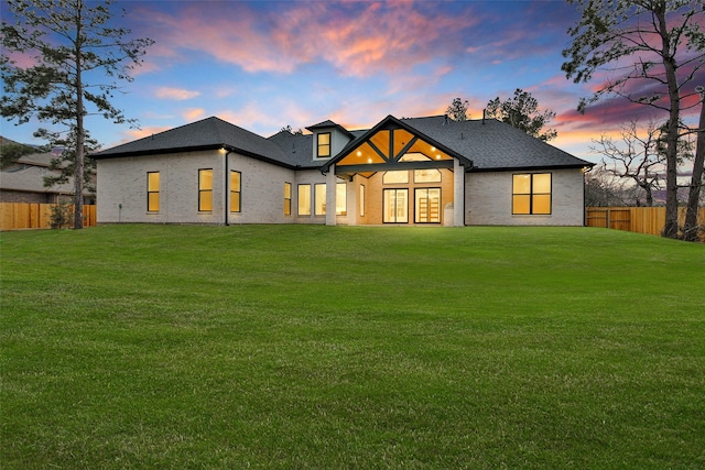 back house at dusk featuring a lawn