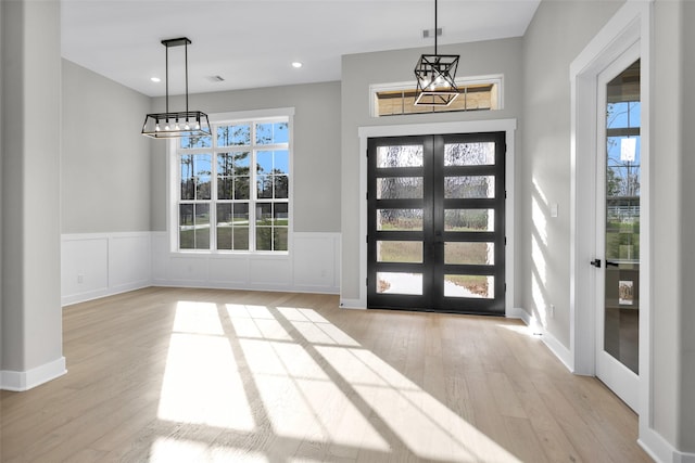 foyer featuring light wood-type flooring, a chandelier, and french doors