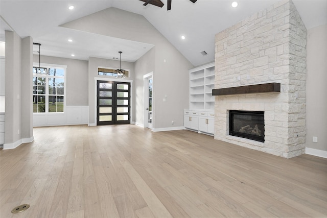 unfurnished living room featuring ceiling fan, a stone fireplace, high vaulted ceiling, and light hardwood / wood-style flooring