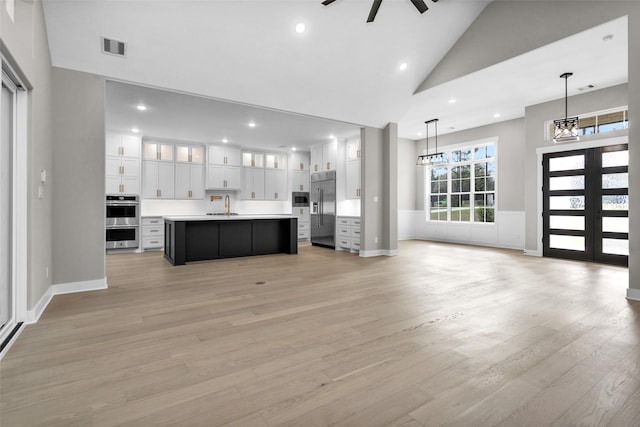 unfurnished living room with sink, ceiling fan with notable chandelier, high vaulted ceiling, and light wood-type flooring