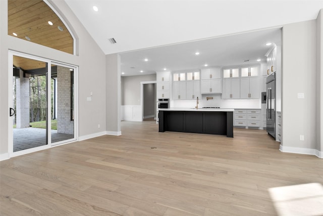 kitchen with stainless steel appliances, a kitchen island with sink, white cabinets, and light hardwood / wood-style floors