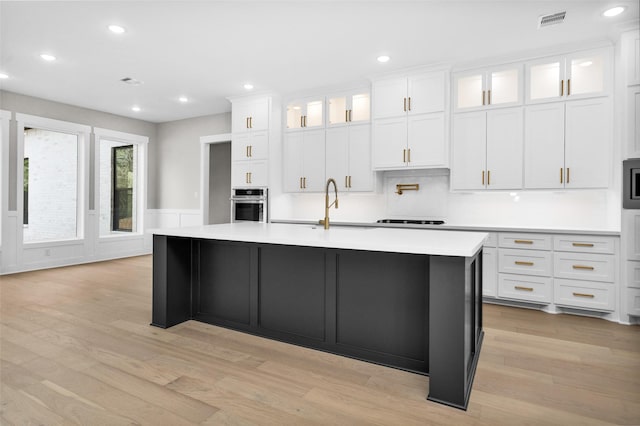 kitchen with sink, light hardwood / wood-style flooring, a kitchen island with sink, stainless steel appliances, and white cabinets