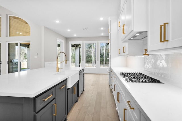 kitchen featuring tasteful backsplash, white cabinets, stainless steel gas cooktop, a center island with sink, and light wood-type flooring