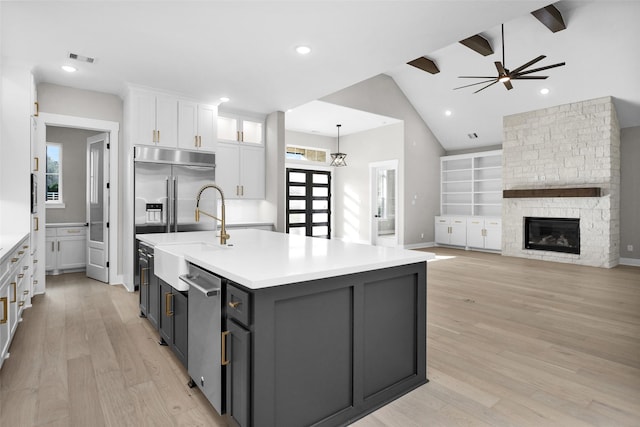 kitchen featuring sink, light hardwood / wood-style flooring, hanging light fixtures, white cabinets, and a center island with sink