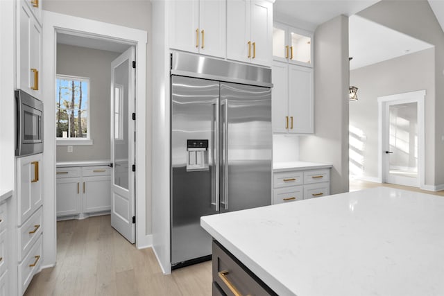 kitchen with pendant lighting, white cabinetry, built in appliances, light stone countertops, and light wood-type flooring