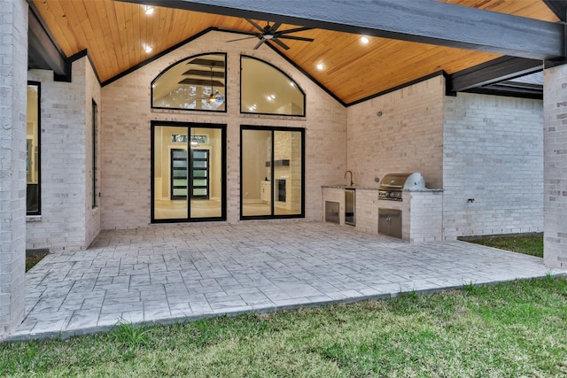 view of exterior entry with ceiling fan, an outdoor kitchen, sink, and a patio area