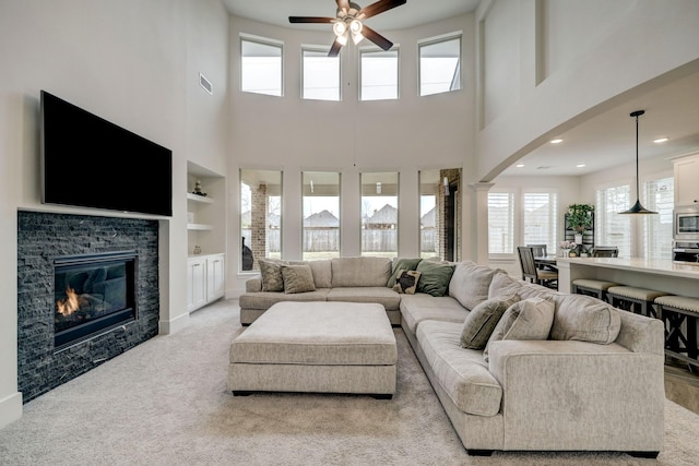 carpeted living room featuring ceiling fan, built in features, and ornate columns