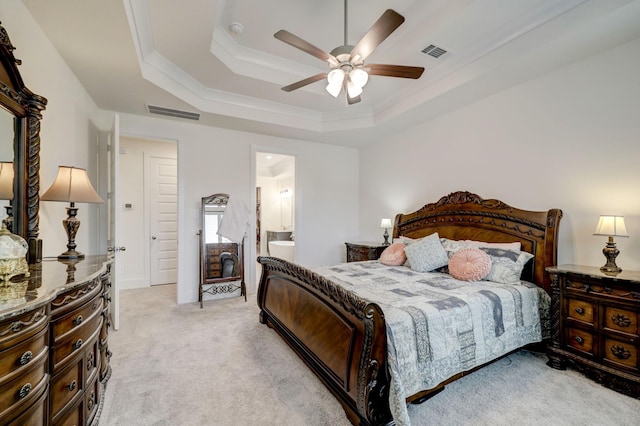 carpeted bedroom with a tray ceiling, ensuite bath, ornamental molding, and ceiling fan