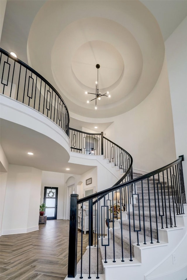 stairs featuring a high ceiling, parquet floors, an inviting chandelier, and a tray ceiling