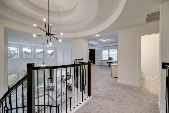 corridor featuring a raised ceiling, light colored carpet, and a chandelier