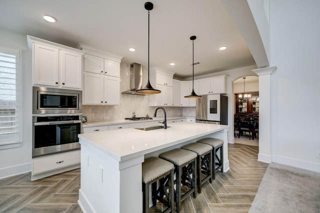 kitchen featuring wall chimney exhaust hood, sink, white cabinetry, decorative light fixtures, and stainless steel appliances