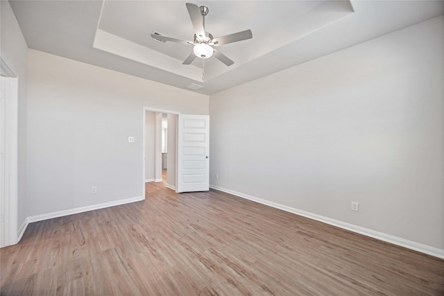 empty room with light hardwood / wood-style flooring, a raised ceiling, and ceiling fan