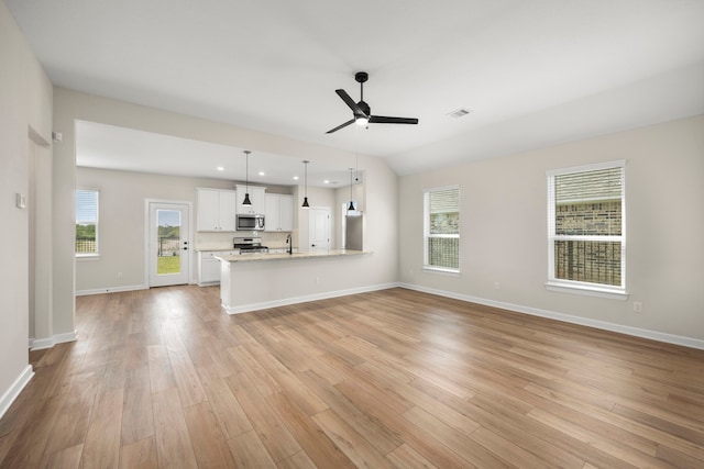 unfurnished living room featuring lofted ceiling, plenty of natural light, ceiling fan, and light wood-type flooring