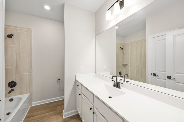 bathroom with hardwood / wood-style flooring, tiled shower / bath, and vanity