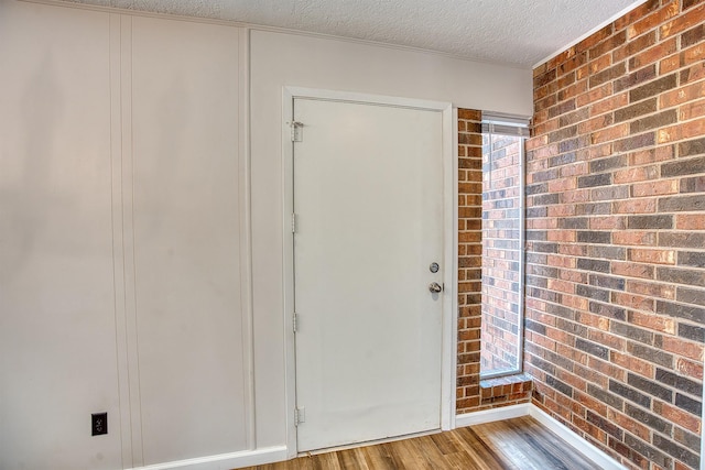 entryway with brick wall, hardwood / wood-style floors, and a textured ceiling