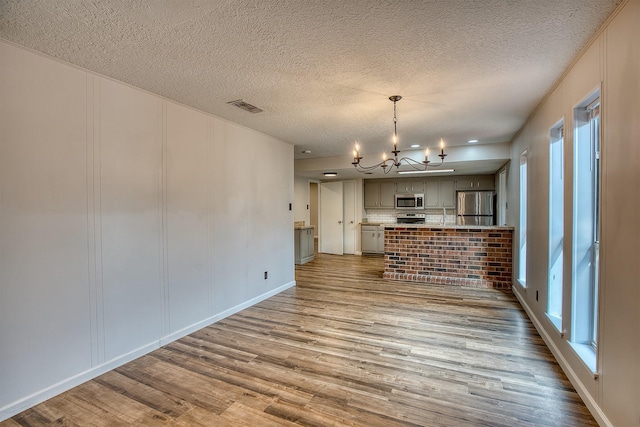 kitchen featuring gray cabinets, a chandelier, hardwood / wood-style flooring, stainless steel appliances, and a textured ceiling