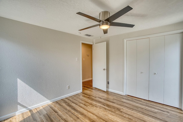 unfurnished bedroom featuring ceiling fan, a closet, light hardwood / wood-style flooring, and a textured ceiling