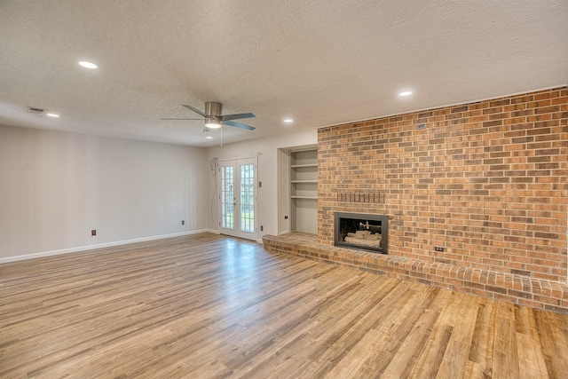 unfurnished living room with built in features, a fireplace, light hardwood / wood-style floors, a textured ceiling, and french doors