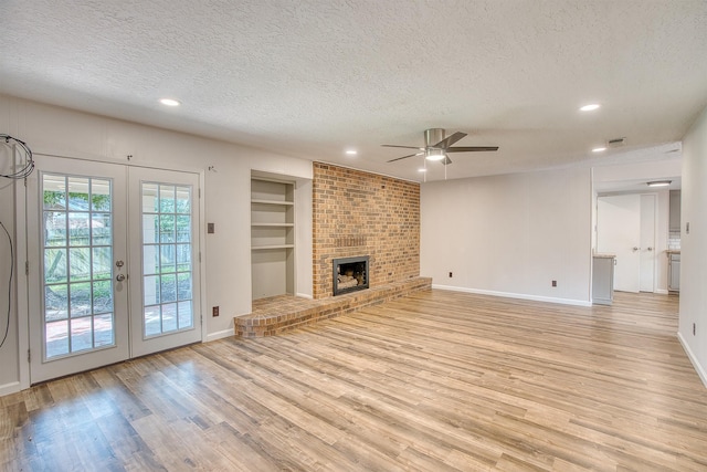 unfurnished living room with built in shelves, a fireplace, light hardwood / wood-style floors, and a textured ceiling