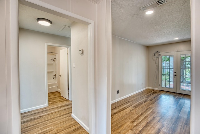 interior space featuring a textured ceiling, light wood-type flooring, and french doors