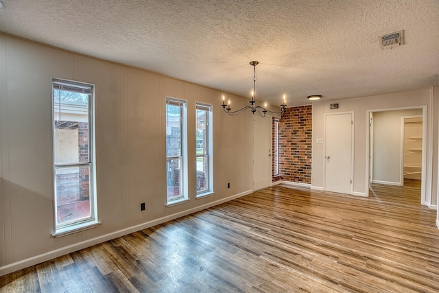 unfurnished dining area featuring an inviting chandelier, a textured ceiling, and light hardwood / wood-style floors