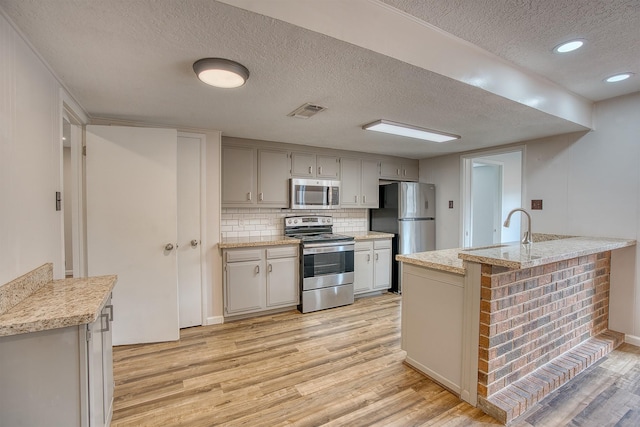 kitchen with appliances with stainless steel finishes, a textured ceiling, backsplash, and light wood-type flooring