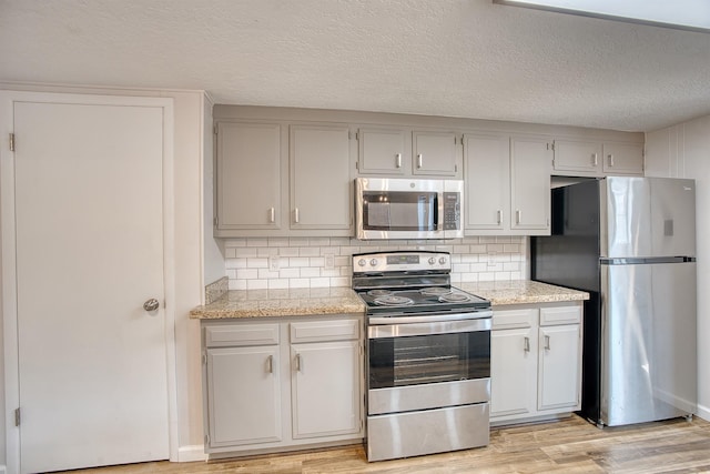 kitchen featuring a textured ceiling, stainless steel appliances, light stone countertops, light hardwood / wood-style floors, and decorative backsplash