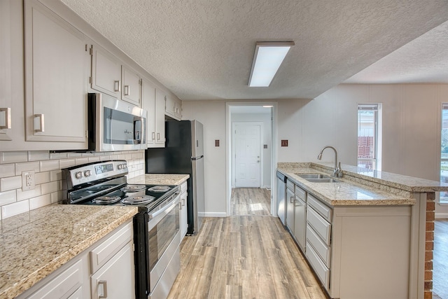 kitchen with sink, light wood-type flooring, appliances with stainless steel finishes, light stone countertops, and decorative backsplash