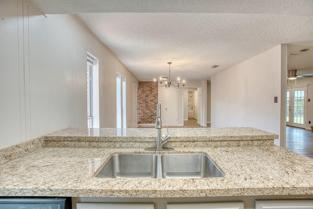 kitchen with sink, hanging light fixtures, light stone countertops, a textured ceiling, and an inviting chandelier